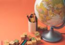 A globe placed next to colorful pencils and building blocks on an orange background