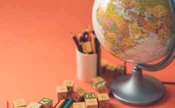 A globe placed next to colorful pencils and building blocks on an orange background