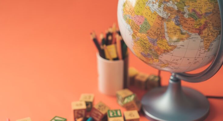 A globe placed next to colorful pencils and building blocks on an orange background